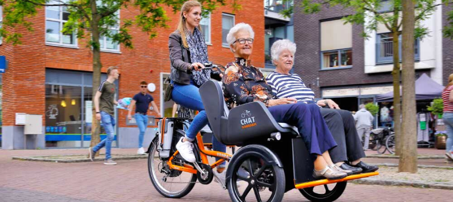 Eine Frau transportiert zwei ältere Personen mit einem Rikscha Dreirad