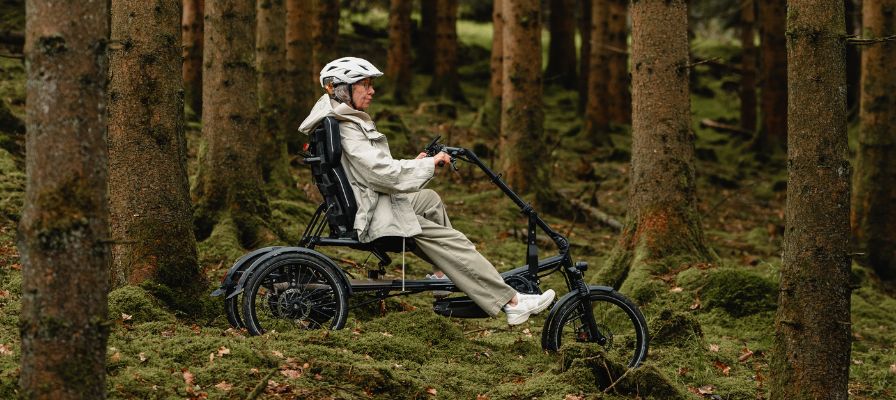 Eine Frau fährt mit einem Dreirad von HASE durch den Wald